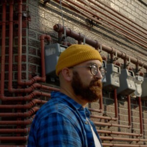 A man in front of a brick wall with many pipes.