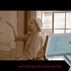 A man in a hat sitting in front of a window.