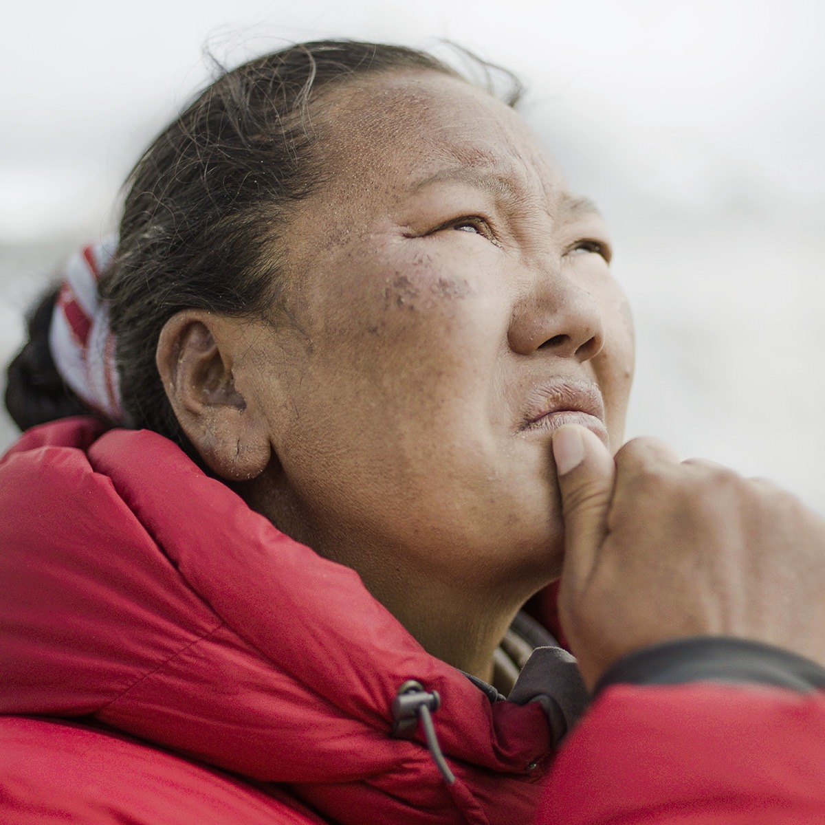 A woman in a red jacket with her hand on her chin.