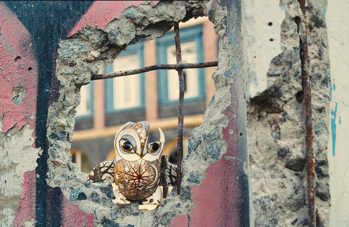 A porcelain owl peeking out of a hole in a wall.